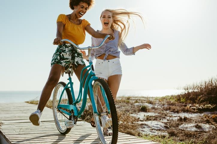 A girl teaching her friend to ride a bicycle near a beach
